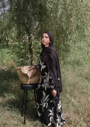 Women's black maxi dress with white leaf print, flowy long-sleeve design, nature-inspired modest fashion piece.